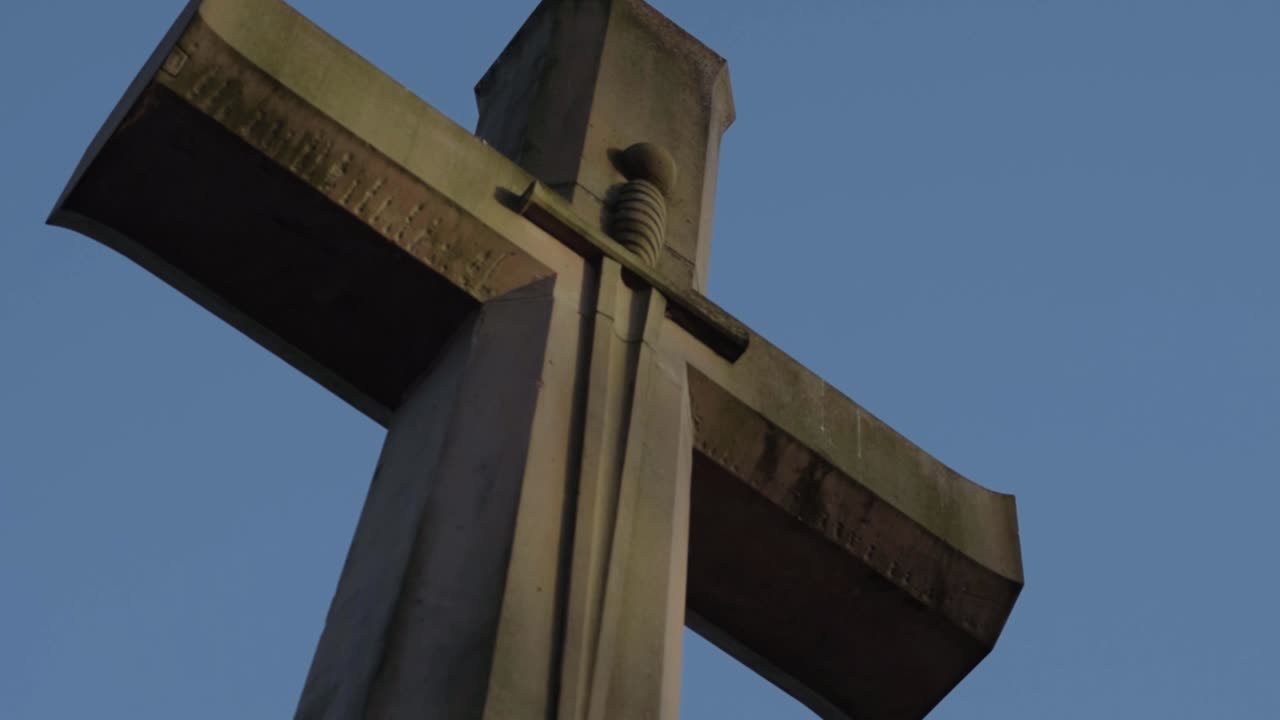Large stone carved cross against blue sky close up tilting shot