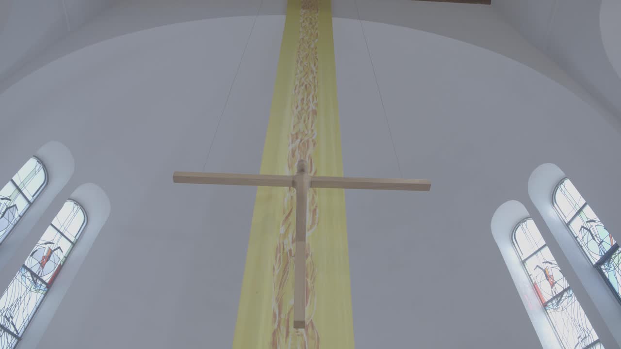 A wooden cross hangs in a church in front of a yellow banner at Easter time
