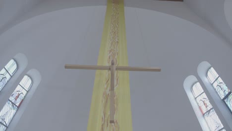 a wooden cross hangs in a church in front of a yellow banner at easter time
