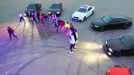 party at the drifting field. young happy people dancing near the race cars outdoors at dusk. top view.