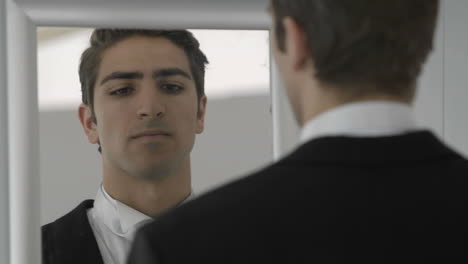 nervous groom looking to mirror adjusting tie