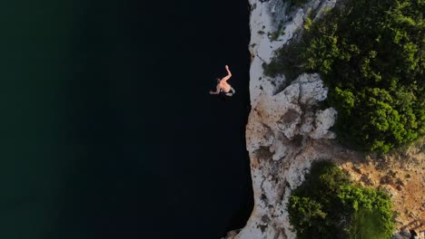 man running on top of cliff and jumping to the water