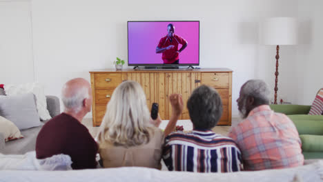 senior diverse friends watching tv with african american male rugby player catching ball on screen