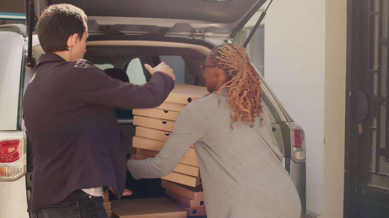 People unloading pizza boxes from a car trunk