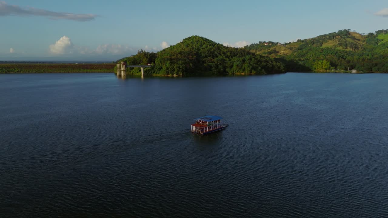 Ferry cruising on Hatillo Dam reservoir at sunset, Dominican Republic. Aerial drone orbiting, copy space