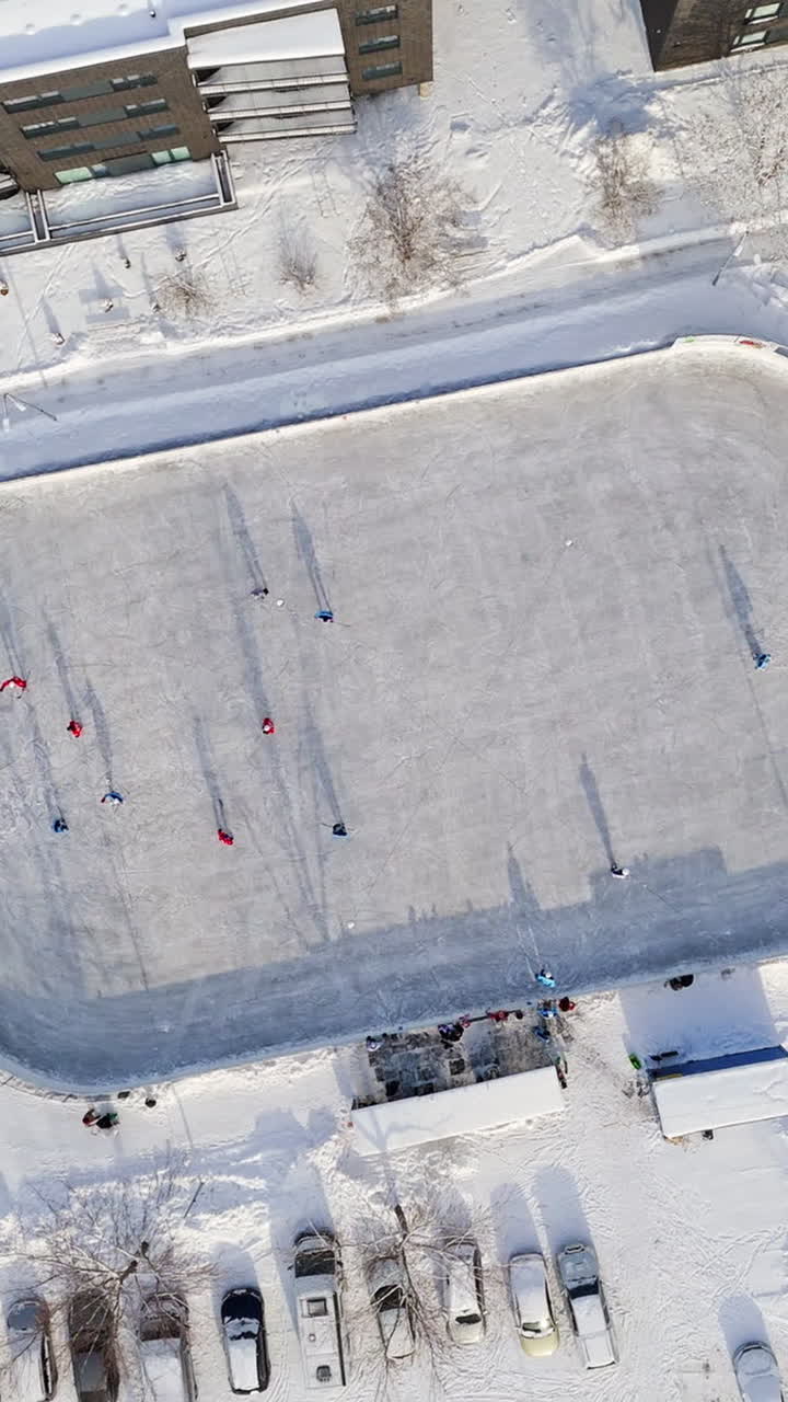 Vertical drone shot rotating above people playing ice hockey at a rink in a city