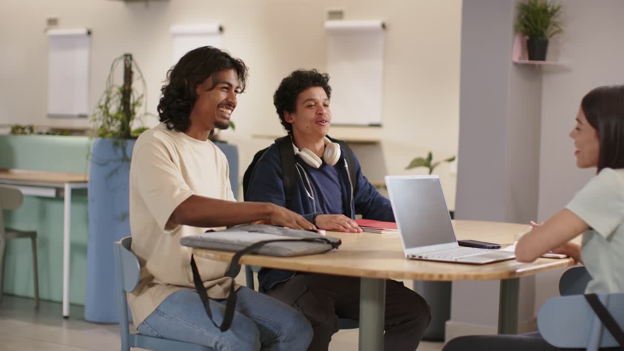 Three classmates laughing and leaning after laptop win on campus, exchanging high-five and cheering