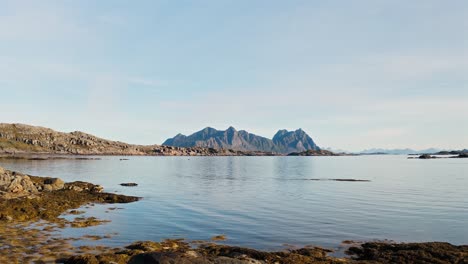 Flying-low,-revealing-the-beautiful-blue-sea-with-gorgeous-mountains-and-a-clear-blue-sky-in-the-background,-Lofoten-Islands,-Norway