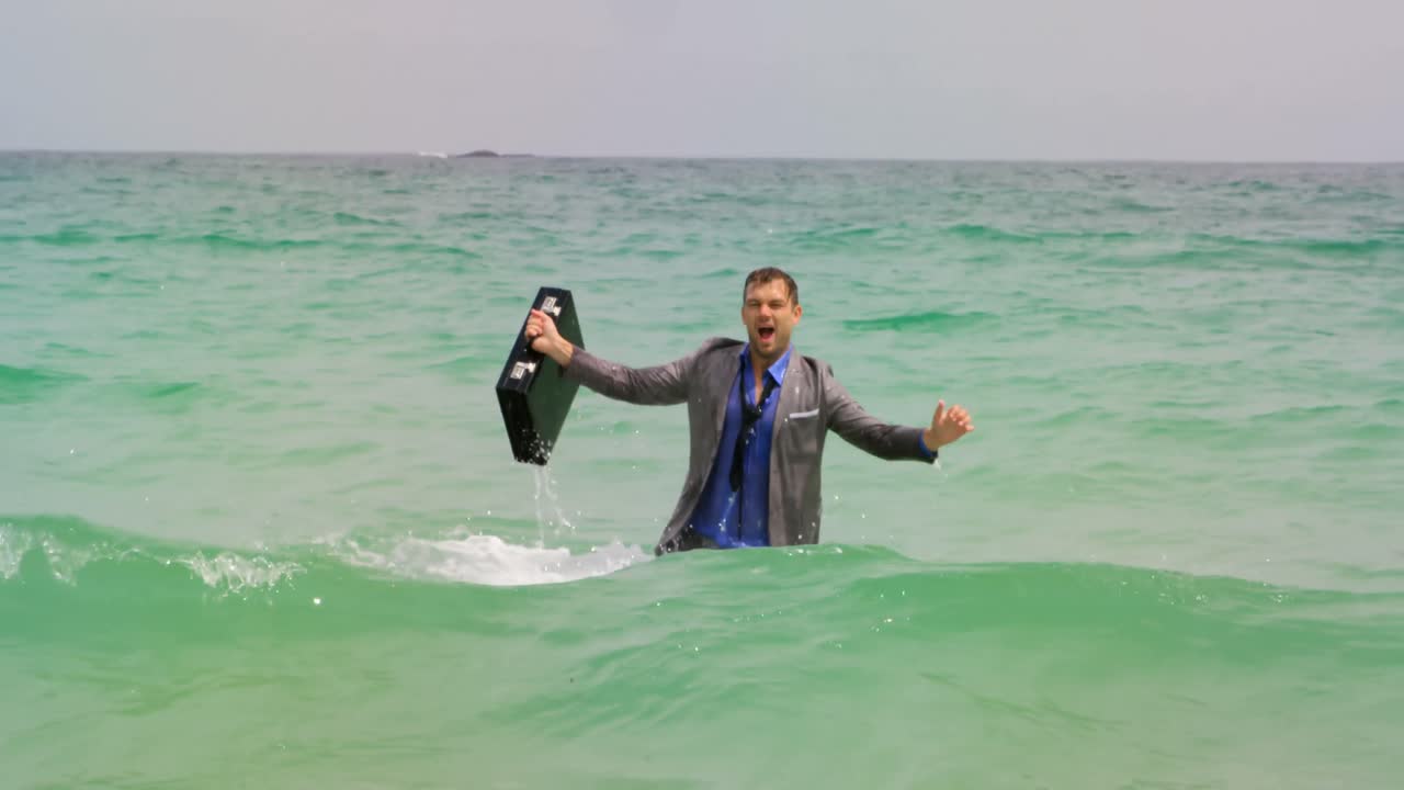 4k 해변에서 브리프케이스를 들고 바다에서 춤추는 백인 사업가의 전면 전망