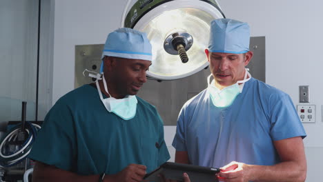 two male surgeons wearing scrubs looking at digital tablet in hospital operating theater