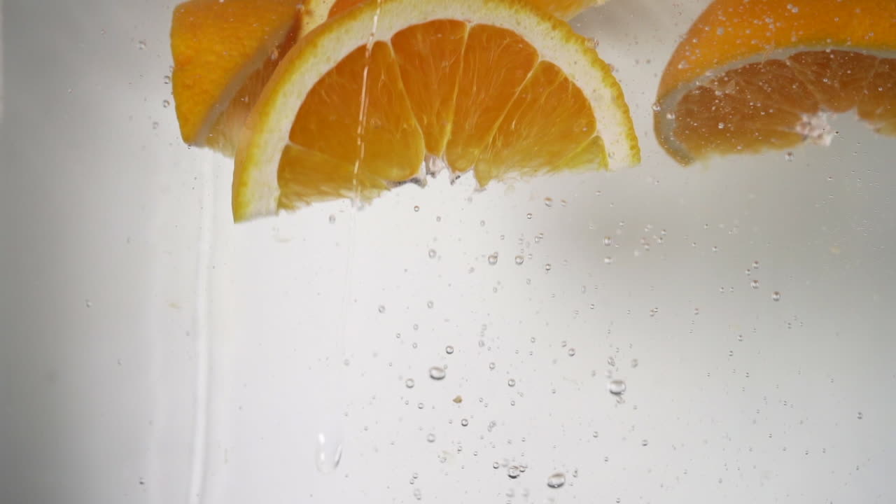 spicchi d'arancia rinfrescanti che cadono nell'acqua, arance fresche di colore arancione vibrante