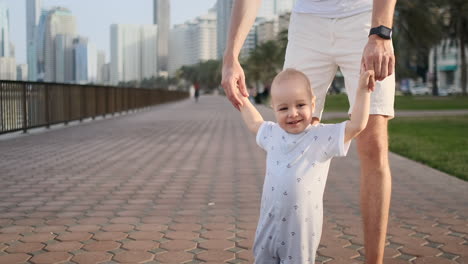 Young-father-with-a-child-and-first-steps.-Young-father-with-a-child-at-outdoor-learninig-for-a-first-steps-near-urban-house-in-the-city