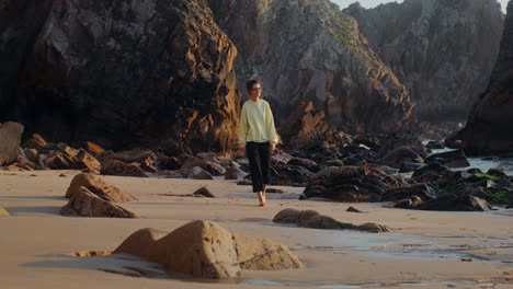 mujer caminando por una playa rocosa al atardecer