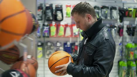 un hombre adulto con chaqueta de cuero negro eligiendo una pelota de baloncesto para deportes al aire libre