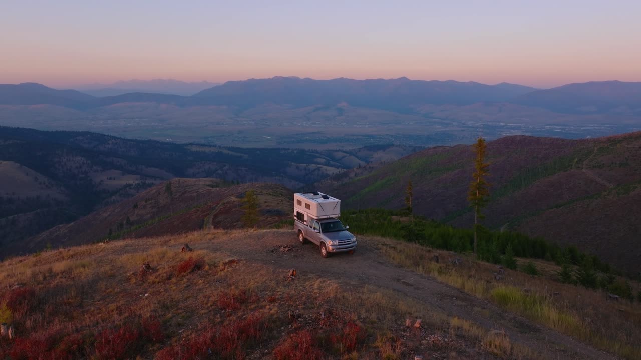 Truck camper parked on mountain ridge above Missoula Montana at dusk, drone ascend reveals perfect campsite