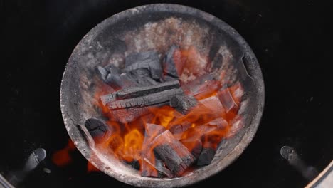 bright orange flames licking and hot charcoal embers glowing in a round barbecue grill, providing heat for cooking or warmth - mesmerizing slow-motion close-up