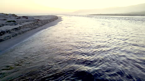 lagoon mouth breaching sandbar to divulge into ocean at sunset