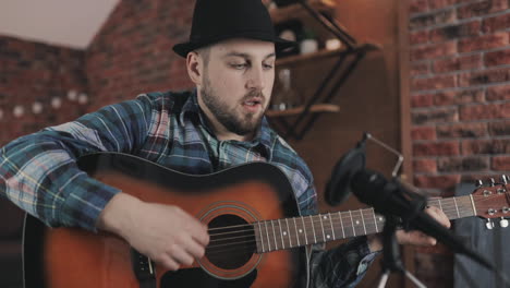 portrait of young male musician playing guitar and singing, recording a song at home