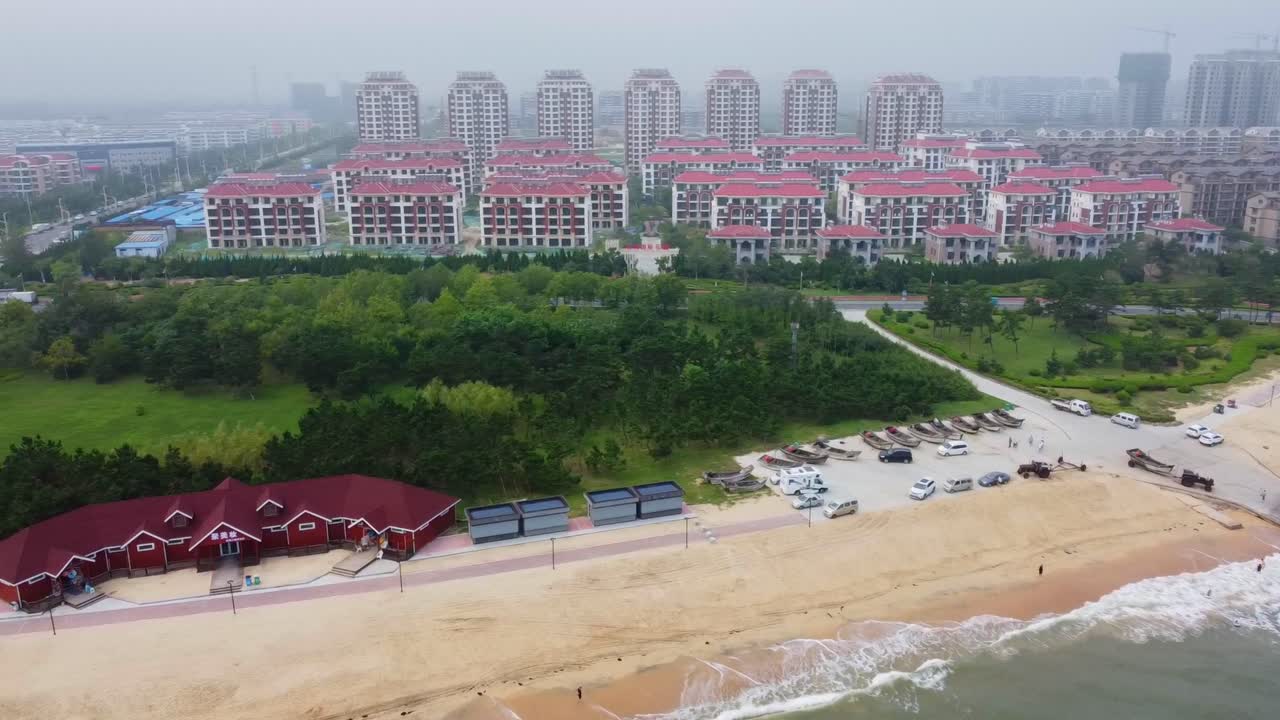 Nanhai Beach and cityscape view from left panning in Nanhai New District, Shandong Province, China. The crowded beach and basket-shaped monument