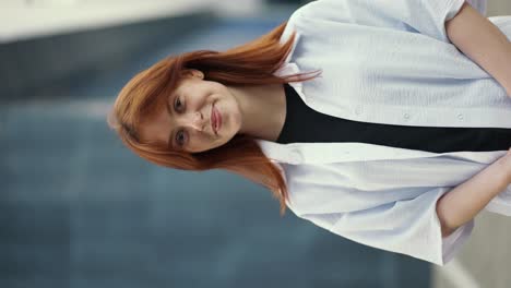 a young girl with a red hair in a white t-shirt smiling and looking straight ahead