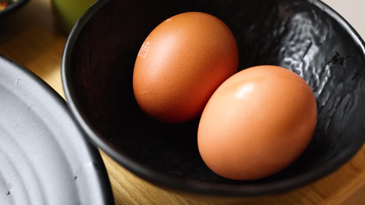 Two fresh brown eggs in a black bowl, natural light, slight camera movement, kitchen setting
