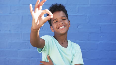 In-a-school-setting,-a-young-African-American-boy-smiles-against-a-blue-background