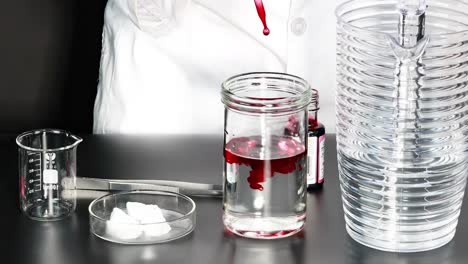 a red liquid is added to a jar of water, observed alongside a beaker and stacked cups.
