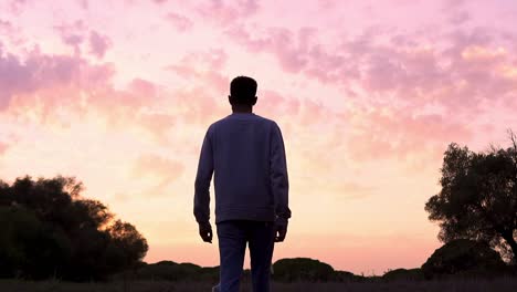 Joven-Caminando-Hacia-Adelante-En-Cámara-Lenta-En-El-Campo-Bajo-Una-Increíble-Puesta-De-Sol-Rosa