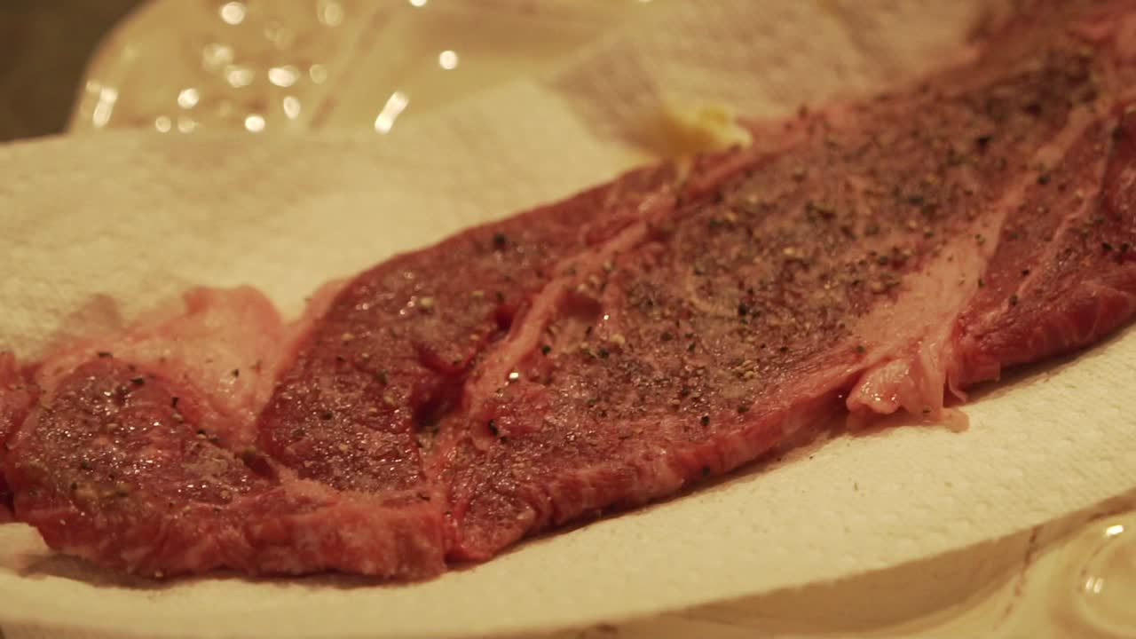 Panning back and forth shot of raw wagyu beef steak being seasoned and prepped for cooking. Slow Motion HD 1080p 23.98p