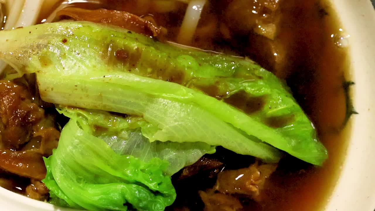 A detailed view of fresh lettuce and herbs in a rich noodle broth.