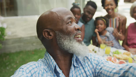 Portrait-of-happy-african-american-family-taking-selfie-and-having-breakfast-in-garden