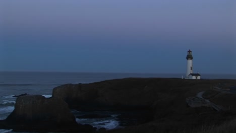 longshot of a white lighthouse with its beacon flashing a warning to sailors