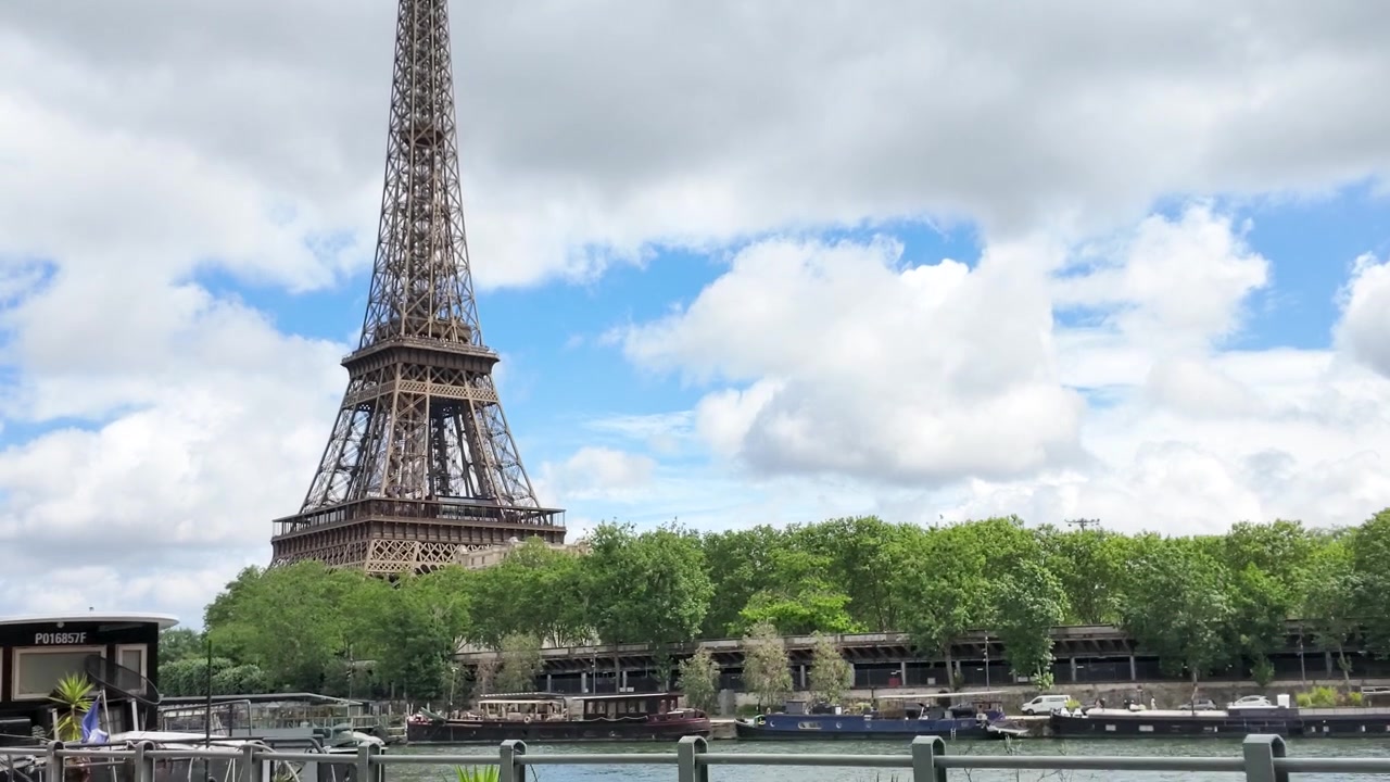 Inquadratura ampia statica della Torre Eiffel a Parigi sotto un cielo luminoso e nuvoloso.