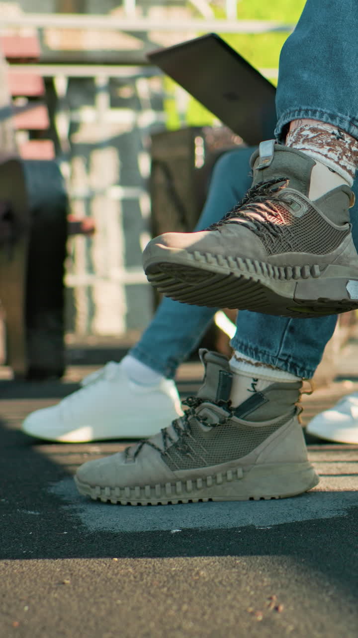 야외에서 나무 벤치에 앉아있는 두 사람의 다리의 클로즈업, 캐주얼 스니커와 청바지를 입고, 빛이 그림자와 초록색을 배경으로 볼 수 있습니다.