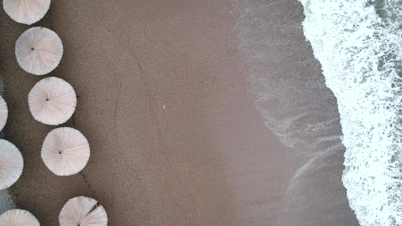 vista aérea de las olas, playa de arena con sombrillas de caña