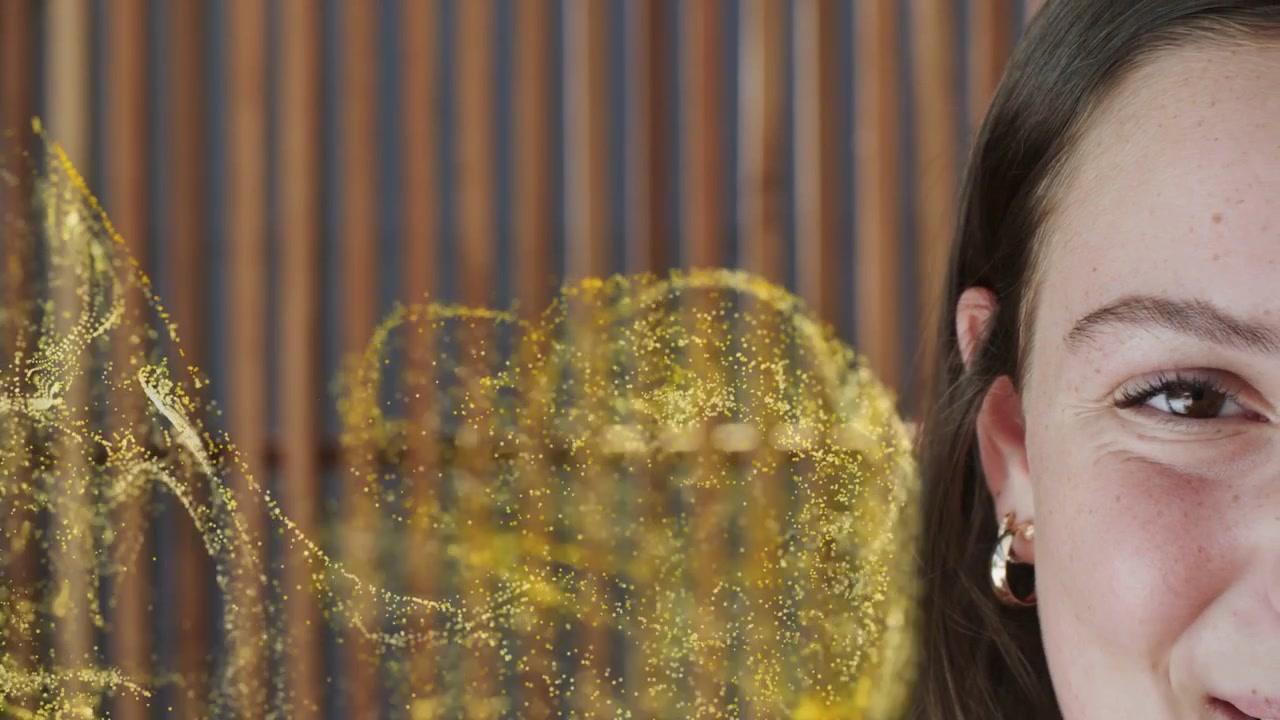 Ragazza adolescente che sorride, particelle d'oro che emergono da sinistra, fluttuando sulla guancia, mostrando una pubblicità di bellezza