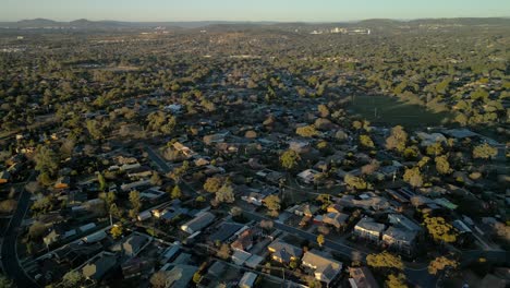 drone arcs around rivett with homes, trees, and the local oval visible below in golden afternoon light