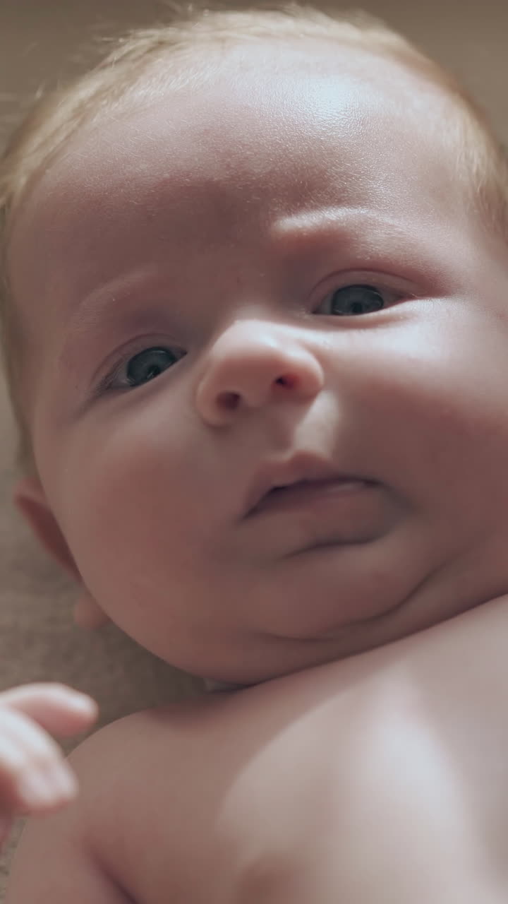 adorable newborn son with cute cheeks and short fair hair lies on baby changing table and smiles extreme close view