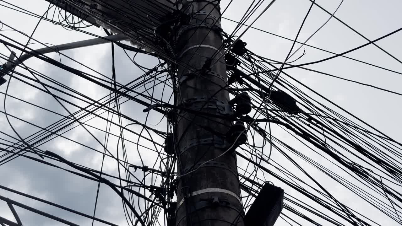 4K image of a utility pole in a poor Brazilian area, overloaded with tangled wires and illegal power connections.