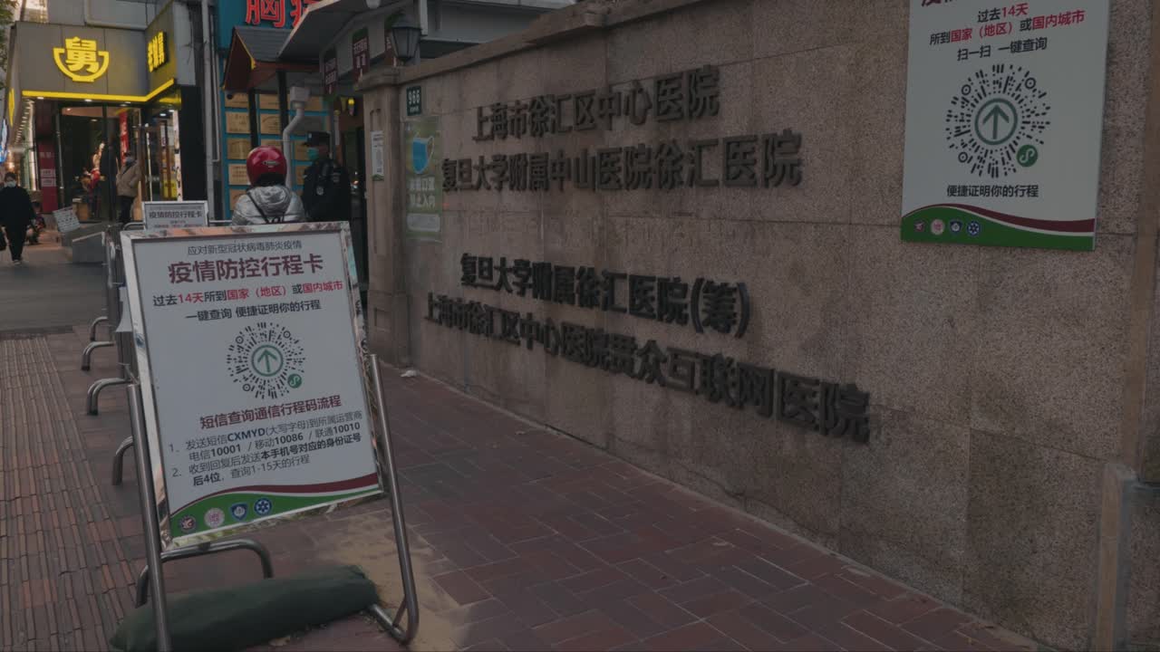 The front entrance of a hospital in Shanghai, China set up during COVID-19 pandemic. Everyone must show green health code before entering. Security guard checking everyone's temperature.
