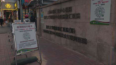 the front entrance of a hospital in shanghai, china set up during covid-19 pandemic. everyone must show green health code before entering. security guard checking everyone's temperature.