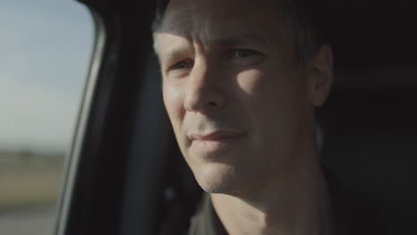 portrait of a man riding passenger side in a car as he turns to look out the window