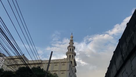 Mosque-minaret-tower-symbols-of-Islam-during-azan-time,-tilt-down-to-road-full-of-traffic,-day