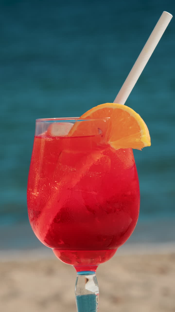 Close up of a refreshing red orange cocktail with orange slice and ice cubes, captured outdoors on a sunny day in Cannes. Vertical