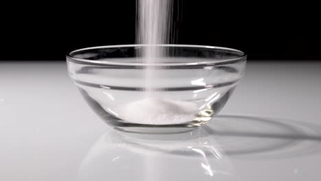 Slow-motion-shot-of-some-sugar-being-poured-into-a-small-glass-bowl-with-a-dark-background