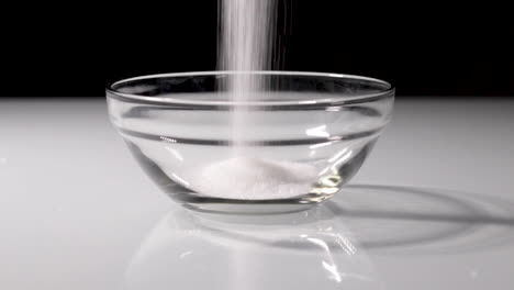 slow-motion shot of some sugar being poured into a small glass bowl with a dark background