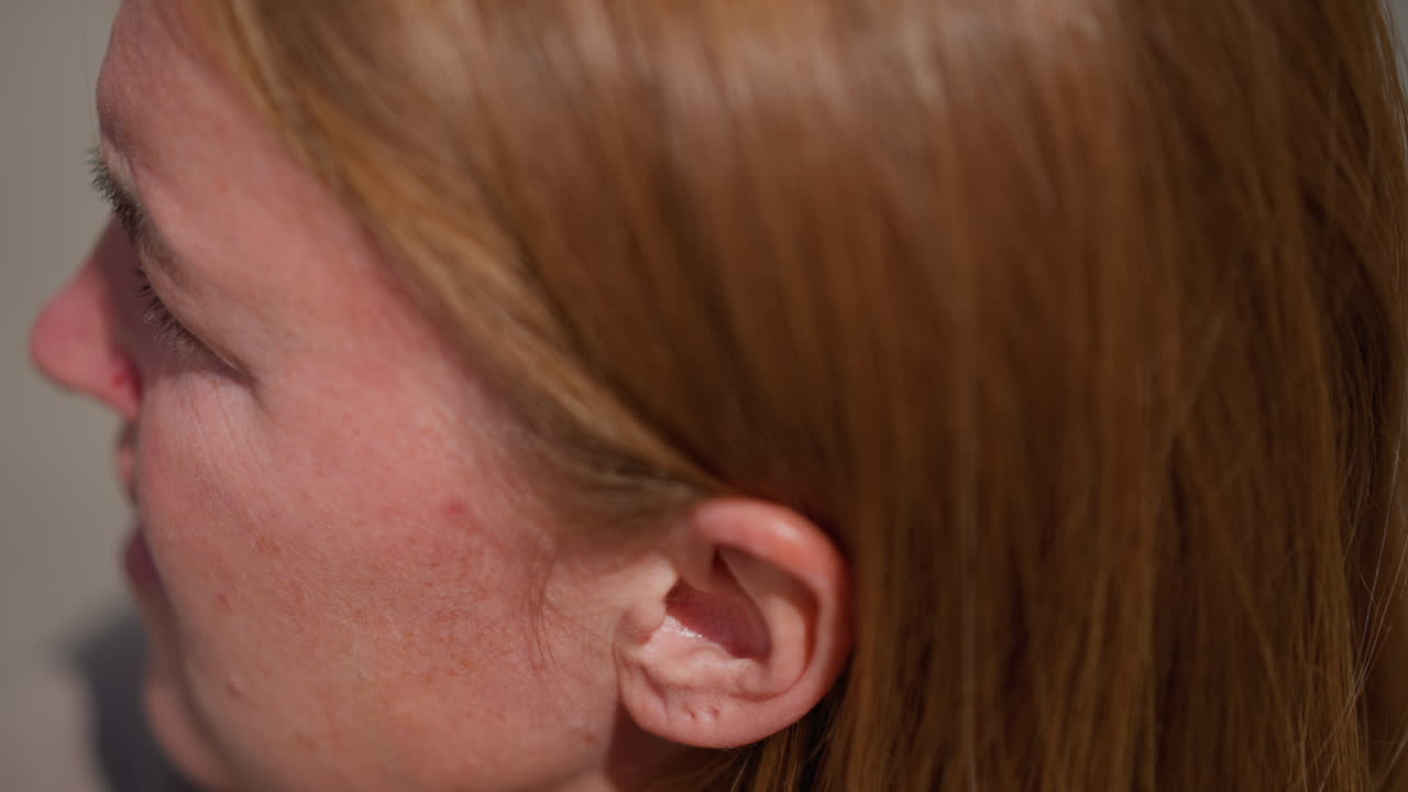 Close up head view of woman with golden hair gently adjusting hair under light, showing smooth strands and subtle motion, focus highlights natural shine and texture