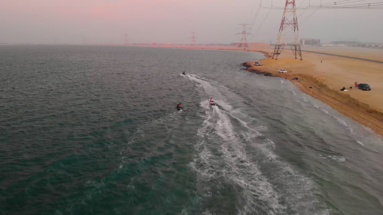 Three Jet Skis Soar across the Green Waters of the Persian Gulf next to White and Red Electrical Pylons