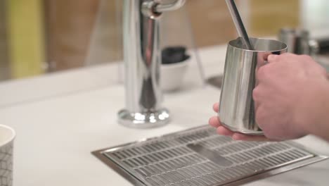 steam rises from metal grate as silver pitcher is placed below spout