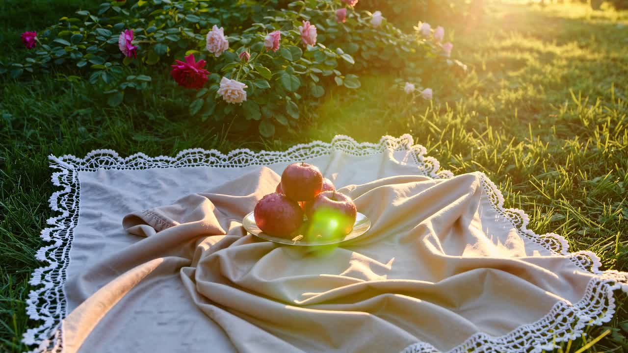 Aerial view of a picnic setup with apples on a lace-trimmed cloth in a garden